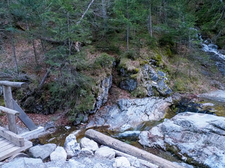 Picturesque Mountain Stream Cascading Over Mossy Rocks with Wooden Bridge in Dense Spring Forest