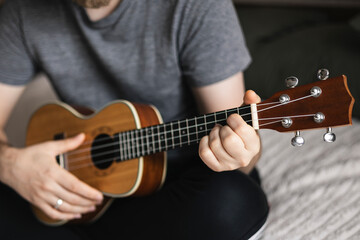 Fototapeta premium Man learns to play the ukulele. The concept of online learning, home education.