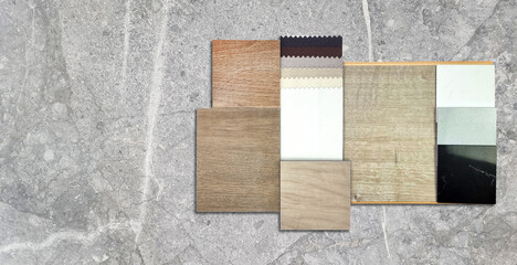 top view of interior material samples including wooden ceramic tiles, real wood laminate flooring tile, palette of solid acrylics, drapery fabric catalog placed on grey marble table with blank space.