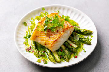 Fried cod with asparagus and on plate. Grey background. Close up.