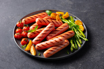Sausages with roasted cherry tomatoes, potatoes and asparagus on a plate. Dark background. Close up.