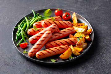 Sausages with roasted cherry tomatoes, potatoes and green bean on a plate. Dark background. Close up.