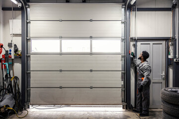 Full length of interracial auto mechanic worker opening garage door in auto mechanic workshop.
