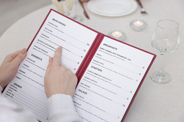Fototapeta premium Woman with menu at table in restaurant, closeup