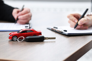 Salesman and client signing documents at wooden table, focus on car model and key. Buying auto