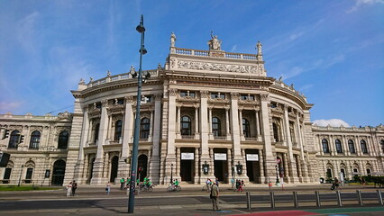 Fototapeta premium The iconic facade of the Burgtheater while cyclists and pedestrians enjoy a sunny day