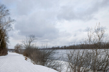 View across a river in winter, snow on river banks, cloudy, nobody