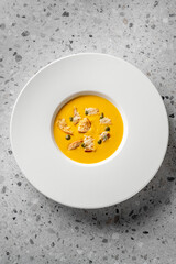 A creamy yellow soup served in a white bowl, garnished with crispy bread pieces and green peas, set on a textured surface. Perfect for culinary or food photography.
