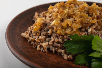 Traditional buckwheat porridge with caramelized onions on a rustic plate. A hearty, nutritious and aromatic dish, popular in Eastern European cuisine, on a clay plate, on a white background