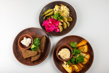 Traditional Eastern European cuisine served on rustic clay plates. A variety of homemade dishes including meat, potatoes, pancakes, dumplings and grilled vegetables, on a light background