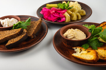 Traditional Eastern European cuisine served on rustic clay plates. A variety of homemade dishes including meat, potatoes, pancakes, dumplings and grilled vegetables, on a light background