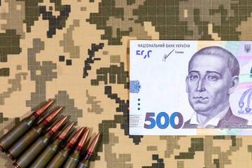 A cartridge from a machine gun and Ukrainian hryvnia on a background of pixel camouflage uniforms...
