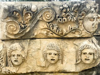 Ancient Roman Stone Relief With Carved Faces And Floral Motifs, Discovered Outdoors In Turkey, Daytime Scene, Represents Heritage, Culture, History, And Artistic Expression In Architecture