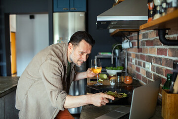 Man cooking at home while watching recipe on laptop