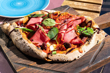pizza on rye dough with pastrami, sun-dried tomatoes, olives, spinach and balsamic vinegar