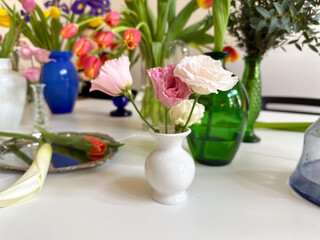 Pink and white lisianthus flowers in small white vase among colorful tulip arrangements. Home decoration and floral composition