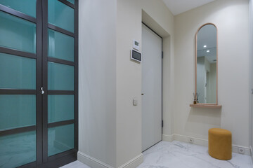 An entrance hall with a minimalistic interior design. A mirror with a shelf and a small ottoman. A...