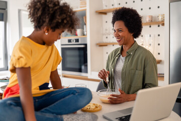 Obraz premium Playful African Mother and Daughter Cooking Together in a Bright Kitchen Setting