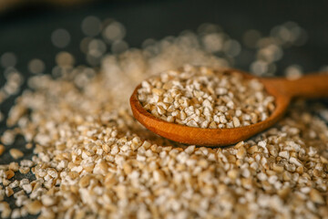 Close-up of raw steel-cut oats in a wooden spoon with scattered grains on a dark surface. Rustic and healthy food concept with soft focus and warm tones
