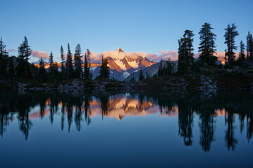 Fototapeta premium Tranquil Mountain Lake at Sunrise with Snow-Capped Peaks and Forest Reflections in Still Water