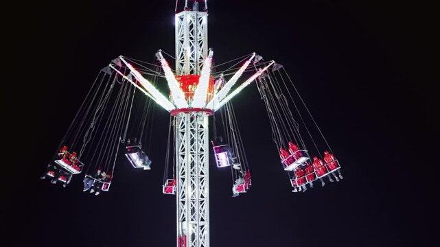 Spinning adrenaline ride with illuminated chain swings rotating high at night