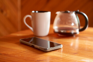 Coffee brewing in modern coffee maker on rustic wooden surface, ceramic mug and smartphone positioned nearby, conveying peaceful morning lifestyle and relaxation moment