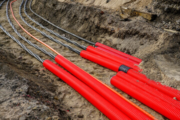 Laying new underground high-voltage power cable in red corrugated protective tube