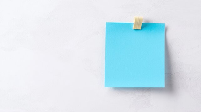 Flat lay of a blue sticky note hanging on a white wall. the note is rectangular in shape and has a yellow paperclip attached to it.
