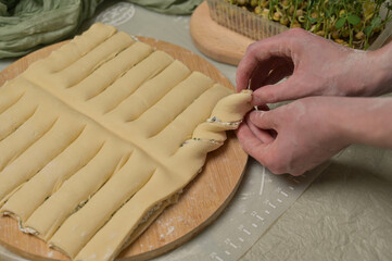 Close up woman's hands twists dough strips on wooden board. Green towel, microgreens sprouts on kitchen table. Home cooking baking puffs