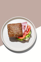 Toast sandwich made of grain bread with prosciutto, tomatoes, lettuce and sauce on brown yellow background