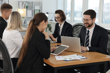 Coworkers with different devices working together at wooden table in office