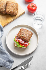 Toast sandwich made of grain bread with prosciutto, cheese, tomatoes, lettuce and sauce on a plate