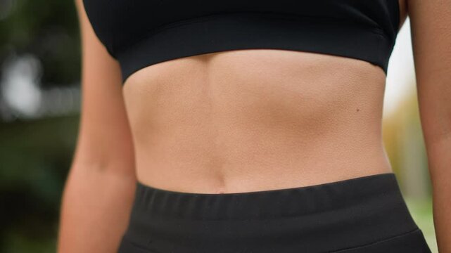 Close-up view of a woman's stomach with goosebumps as she breathes in deeply, showing her physical response to a deep breath while wearing black workout gear, focusing on her midsection