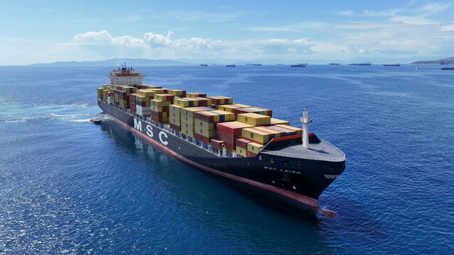 Aerial drone photo of MSC truck size container cargo vessel cruising in deep blue sea near commercial port of Piraeus