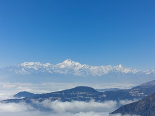 Majestic view of the Kanchenjunga mountain range, also known as Sleeping Buddha, standing tall above the clouds under a clear blue sky. A stunning natural marvel of the Eastern Himalayas.