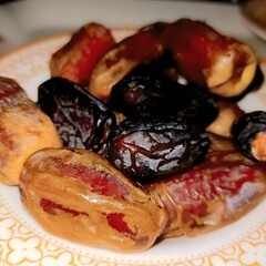 A close-up of Medjool dates on a floral plate, showcasing their soft, wrinkled texture and rich brown hues. Known for their sweetness and nutrition, these dates are a popular snack.