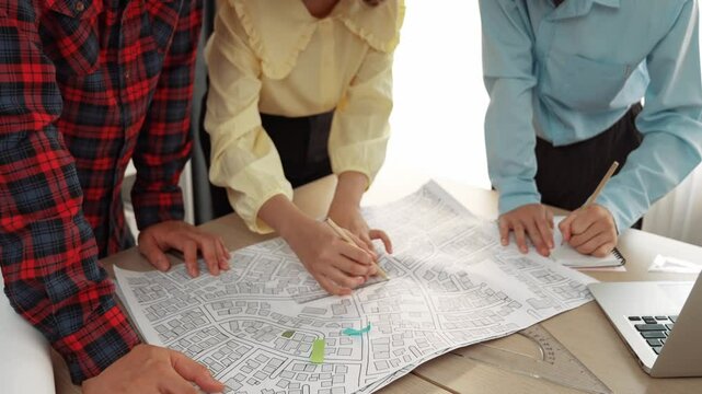 Professional engineer team discussion about house design on meeting table with architectural equipment and building blueprint scatter around at modern office. Focus on hand. Closeup. Delineation.