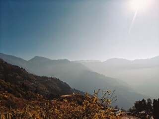 Serene mountain landscape bathed in golden sunlight with layered ridges fading into mist. Captivating view of a tranquil sunrise over hills, ideal for nature, travel, and wellness themes.