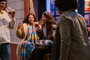 Group of four friends standing and sitting while laughing and holding cups, outdoors, on a walk
