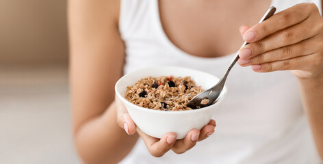 Closeup of bowl with fresh oatmeal and spoon in woman hands, healthy and nutritive breakfast concept. Unrecognizable lady holding delicious homemade granola, having breakfast at home