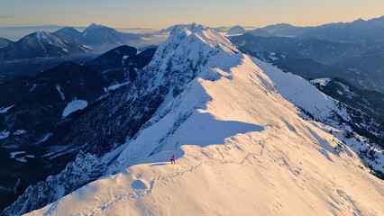 An aerial view of a snow-covered mountain peak with a lone climber, highlighting the thrill and beauty of mountaineering.