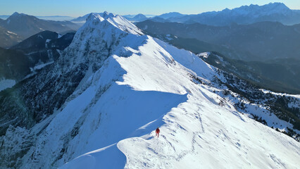 An aerial view of a snowy mountain peak with a lone skier, highlighting the thrill and serenity of...
