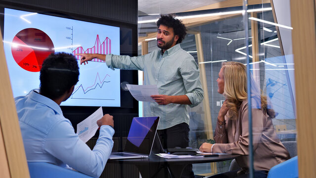 In a modern office, a man presents data on a large screen to a team, highlighting the importance of collaboration and effective communication.