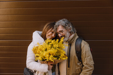 A White elder woman with brown hair, a White elder man with a beard and glasses, smiling together...