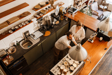 A Caucasian man and woman stand near the wooden countertop of the kitchen corner of a coffee shop and talk. Concept of coffee shop work routine, barista's working day, coffee shop management.