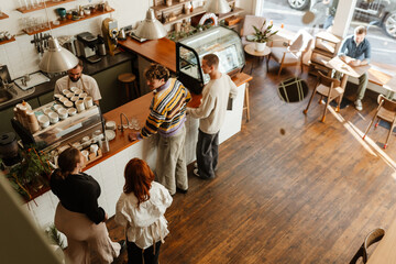 A White male barista serving a group of customers at the counter of a trendy cafe, with a modern coffee machine, casual outfits, and a warm atmosphere in a spacious interior.
