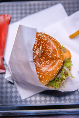 Top view of a delicious burger with sesame seed bun, fresh lettuce and tomato wrapped in paper,...