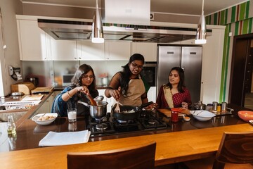 A group of Indian young women cooking dinner together in a modern kitchen, dressed in colorful sarees and aprons, preparing food with spices and fresh ingredients, enjoying their time together.