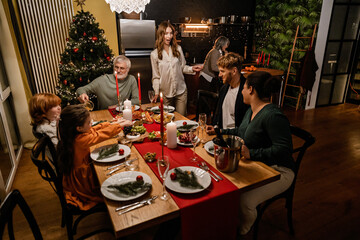 A White big family is celebrating Christmas together around the dinner table, while enjoying a festive meal with laughter, love, and holiday cheer while in a warm, cozy home setting.