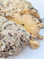 Artisanal aged cheese with rough rind partially sliced on a white plate